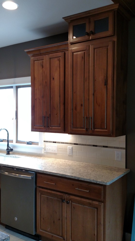 This is an example of a mid-sized country l-shaped kitchen in Indianapolis with a farmhouse sink, raised-panel cabinets, medium wood cabinets, quartzite benchtops, white splashback, subway tile splashback, coloured appliances and vinyl floors.