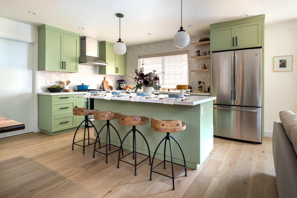 Example of a transitional l-shaped medium tone wood floor and brown floor kitchen design with shaker cabinets, green cabinets, stainless steel appliances, an island, white countertops and quartzite countertops