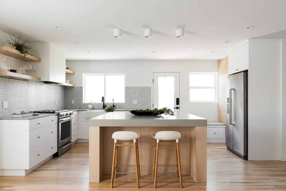 Design ideas for a small scandinavian l-shaped kitchen in Salt Lake City with a farmhouse sink, flat-panel cabinets, white cabinets, quartz benchtops, grey splashback, stainless steel appliances, light hardwood floors, with island, beige floor and grey benchtop.