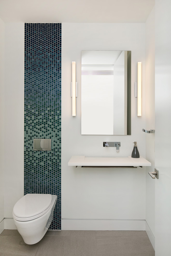 This is an example of a mid-sized contemporary powder room in Tampa with open cabinets, a wall-mount toilet, multi-coloured tile, blue tile, mosaic tile, white walls, porcelain floors, a wall-mount sink, engineered quartz benchtops, grey floor and white benchtops.