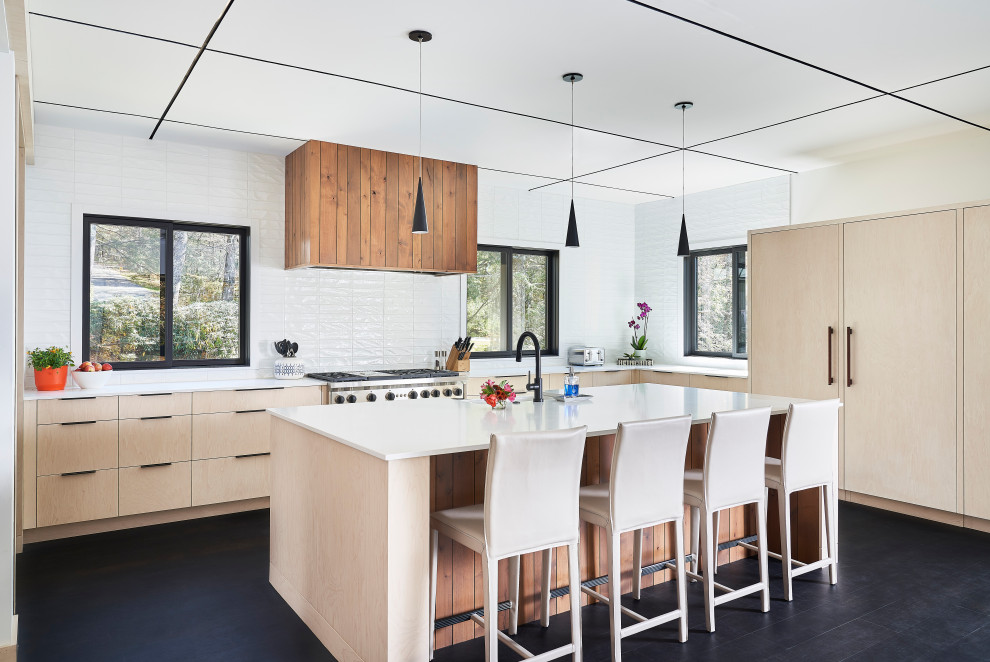 Large country u-shaped eat-in kitchen in Other with flat-panel cabinets, light wood cabinets, quartzite benchtops, white splashback, ceramic splashback, stainless steel appliances, with island, white benchtop, a farmhouse sink and black floor.
