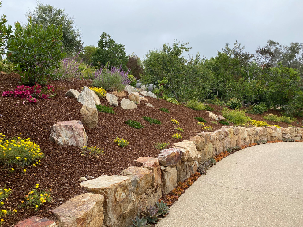This is an example of an expansive mediterranean sloped full sun driveway for summer in San Diego with a retaining wall and natural stone pavers.