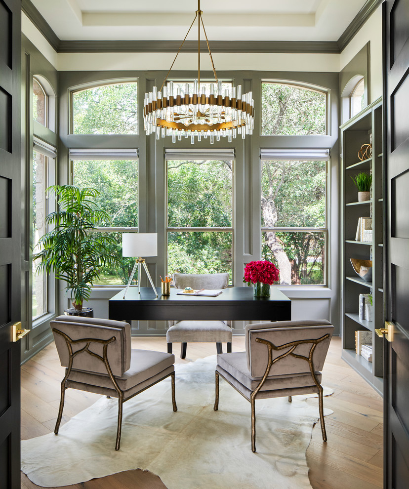 This is an example of a mid-sized transitional home office in Austin with a library, grey walls, light hardwood floors, a freestanding desk and grey floor.