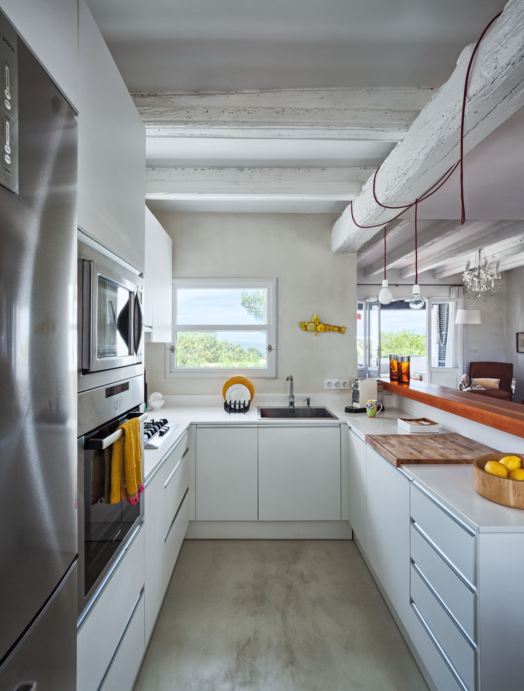 Inspiration for a mid-sized country u-shaped eat-in kitchen in Other with a drop-in sink, flat-panel cabinets, white cabinets, solid surface benchtops, beige splashback, stainless steel appliances, concrete floors and a peninsula.