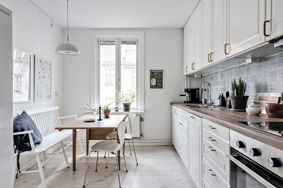 Inspiration for a mid-sized scandinavian single-wall eat-in kitchen in Gothenburg with a double-bowl sink, white cabinets, wood benchtops, ceramic splashback, white appliances, light hardwood floors, no island, blue splashback and raised-panel cabinets.
