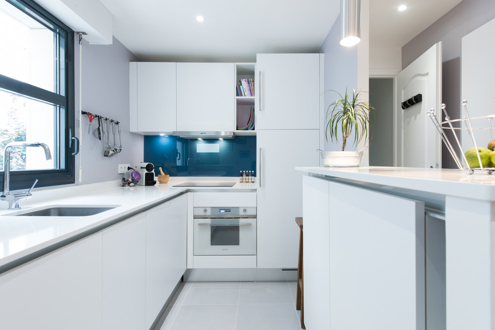 This is an example of a mid-sized modern u-shaped eat-in kitchen in Paris with an integrated sink, beaded inset cabinets, white cabinets, quartzite benchtops, blue splashback, glass tile splashback and panelled appliances.