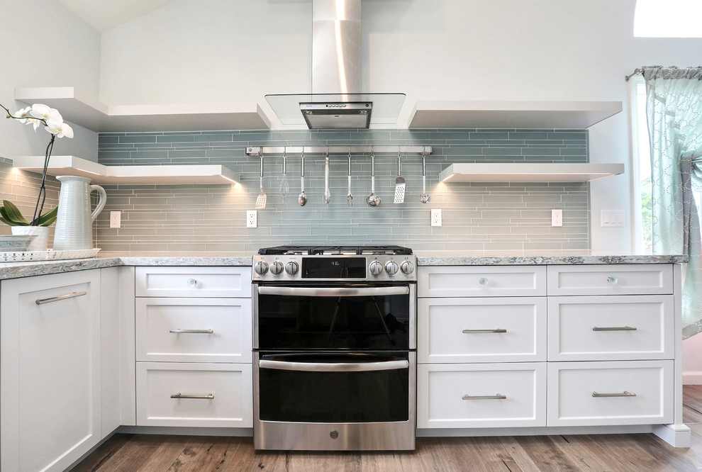 Inspiration for a beach style u-shaped open plan kitchen in Other with a farmhouse sink, shaker cabinets, white cabinets, quartz benchtops, blue splashback, glass tile splashback, stainless steel appliances, medium hardwood floors and brown floor.