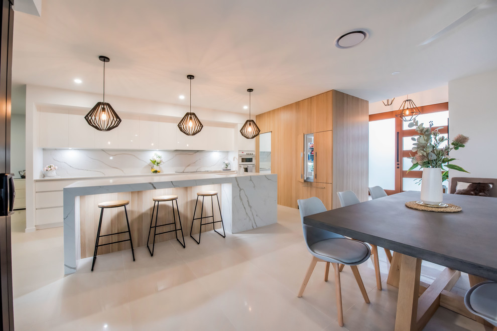 Photo of a large contemporary galley open plan kitchen in Other with an undermount sink, flat-panel cabinets, light wood cabinets, marble benchtops, white splashback, marble splashback, white appliances, ceramic floors, with island, white floor and white benchtop.