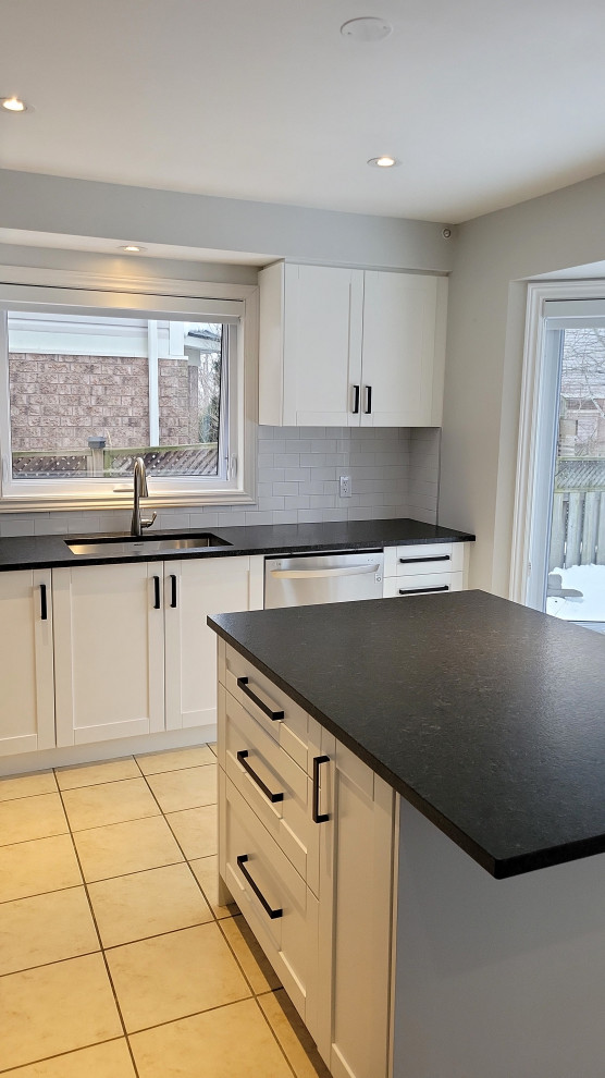 Transitional kitchen photo with an undermount sink, recessed-panel cabinets, white cabinets, granite countertops, gray backsplash, porcelain backsplash and black countertops