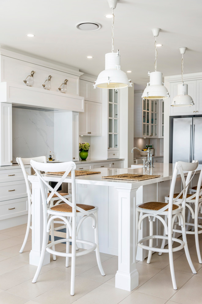 This is an example of a large beach style galley eat-in kitchen in Gold Coast - Tweed with a farmhouse sink, shaker cabinets, white cabinets, marble benchtops, white splashback, marble splashback, stainless steel appliances, ceramic floors, with island, beige floor and white benchtop.