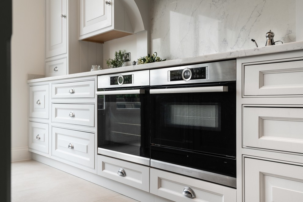 Design ideas for a large traditional l-shaped kitchen in Essex with an undermount sink, raised-panel cabinets, grey cabinets, quartzite benchtops, white splashback, stainless steel appliances, porcelain floors, with island, beige floor and white benchtop.