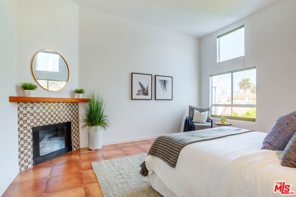 This is an example of a mid-sized contemporary master bedroom in Los Angeles with white walls, terra-cotta floors, a standard fireplace, a tile fireplace surround and orange floor.