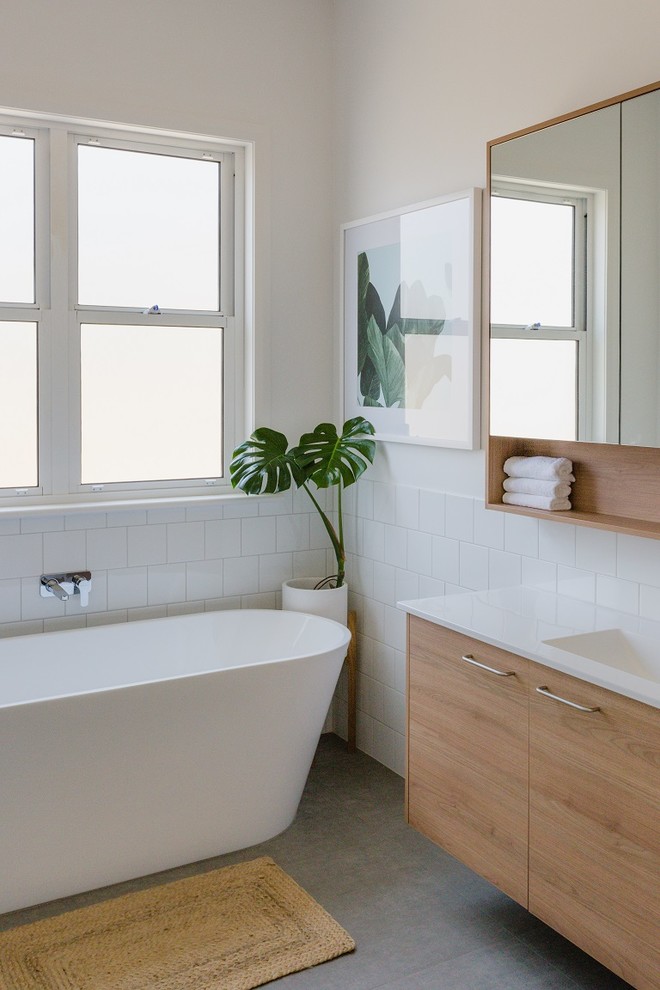 Photo of a large contemporary kids bathroom in Geelong with furniture-like cabinets, light wood cabinets, a freestanding tub, an open shower, a one-piece toilet, white tile, ceramic tile, white walls, ceramic floors, an integrated sink, solid surface benchtops, grey floor, an open shower and white benchtops.
