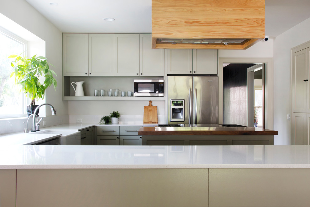 Inspiration for a transitional u-shaped dark wood floor open concept kitchen remodel in Austin with a farmhouse sink, shaker cabinets, green cabinets, wood countertops, white backsplash, stone slab backsplash, stainless steel appliances, white walls and an island
