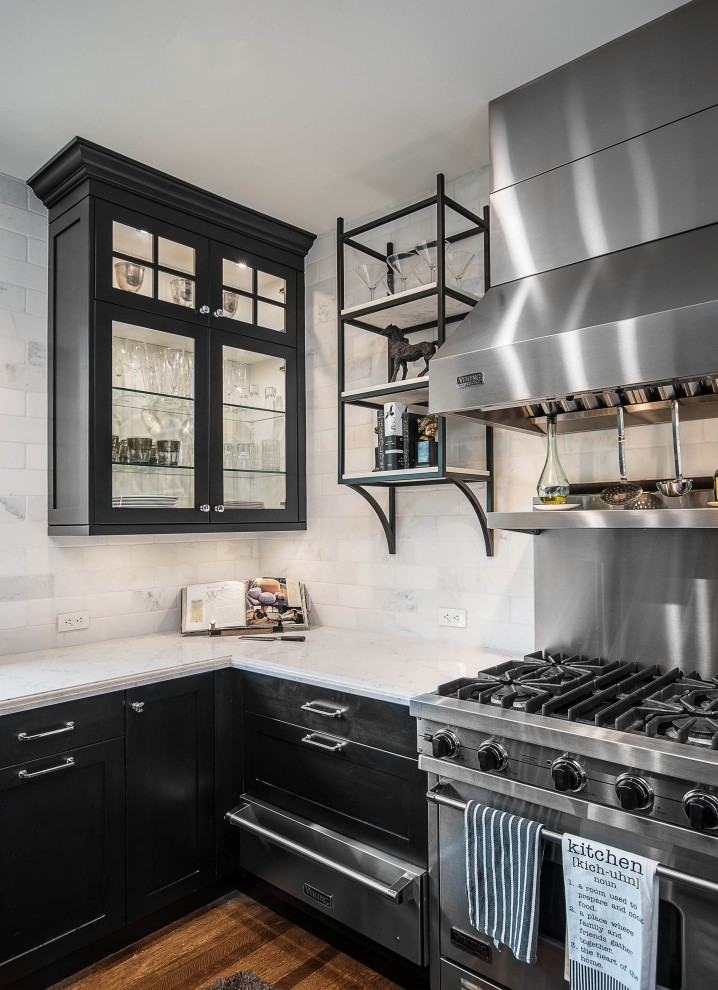 Mid-sized country u-shaped separate kitchen in Los Angeles with a farmhouse sink, stainless steel appliances, a peninsula, brown floor, grey benchtop, glass-front cabinets, black cabinets, grey splashback, subway tile splashback, light hardwood floors and quartz benchtops.