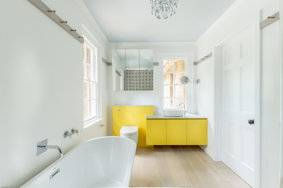 Свежая идея для дизайна: детская ванная комната среднего размера в стиле фьюжн с плоскими фасадами, желтыми фасадами, отдельно стоящей ванной, угловым душем, унитазом-моноблоком, разноцветной плиткой, керамогранитной плиткой, белыми стенами, светлым паркетным полом, настольной раковиной, мраморной столешницей и душем с распашными дверями - отличное фото интерьера