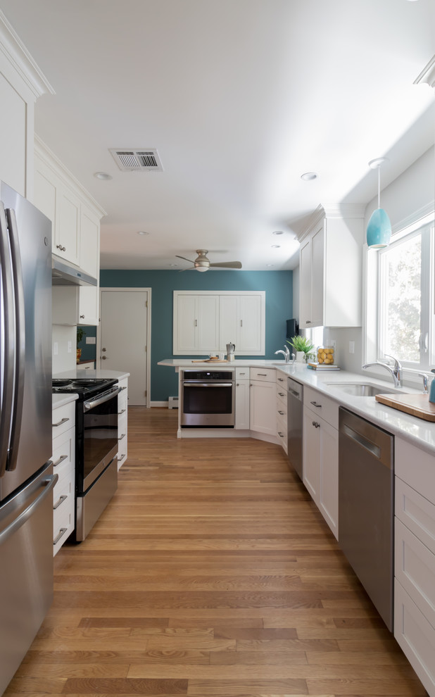 Design ideas for a mid-sized traditional galley eat-in kitchen in Other with an undermount sink, shaker cabinets, white cabinets, quartz benchtops, stainless steel appliances, medium hardwood floors, a peninsula and white benchtop.
