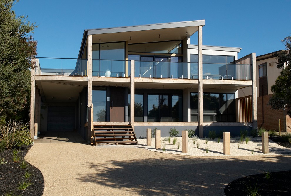 This is an example of a large beach style two-storey glass house exterior in Melbourne with a flat roof and a metal roof.