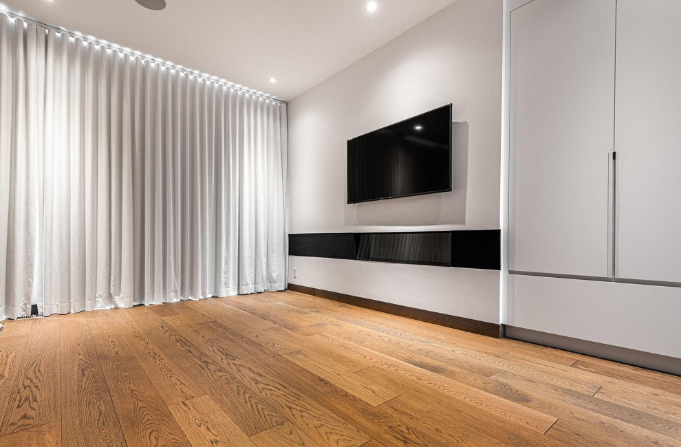 This is an example of a mid-sized contemporary enclosed family room in Toronto with grey walls, light hardwood floors, a wall-mounted tv and brown floor.