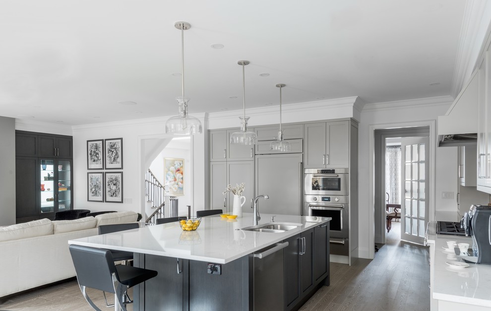 Mid-sized transitional l-shaped eat-in kitchen in Toronto with an undermount sink, shaker cabinets, grey cabinets, quartz benchtops, brown splashback, glass tile splashback, stainless steel appliances, medium hardwood floors, with island, grey floor and white benchtop.