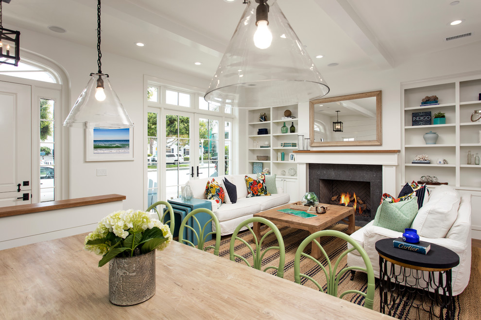 This is an example of a large beach style open plan dining in Orange County with white walls, light hardwood floors, a standard fireplace and a stone fireplace surround.
