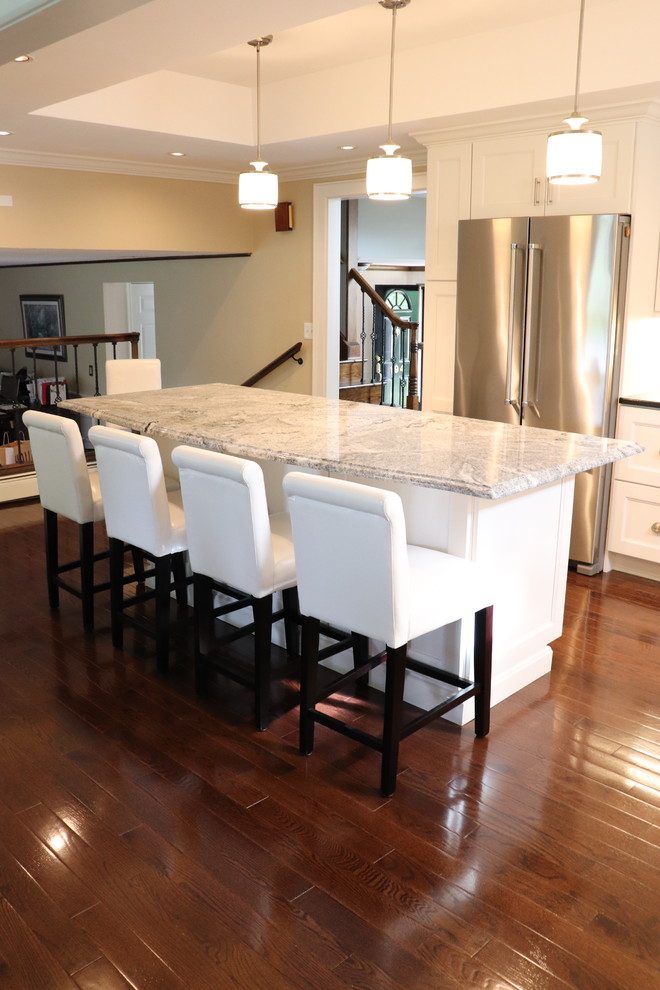 Large transitional l-shaped medium tone wood floor and brown floor eat-in kitchen photo in New York with a double-bowl sink, shaker cabinets, white cabinets, quartzite countertops, beige backsplash, stainless steel appliances, an island and black countertops