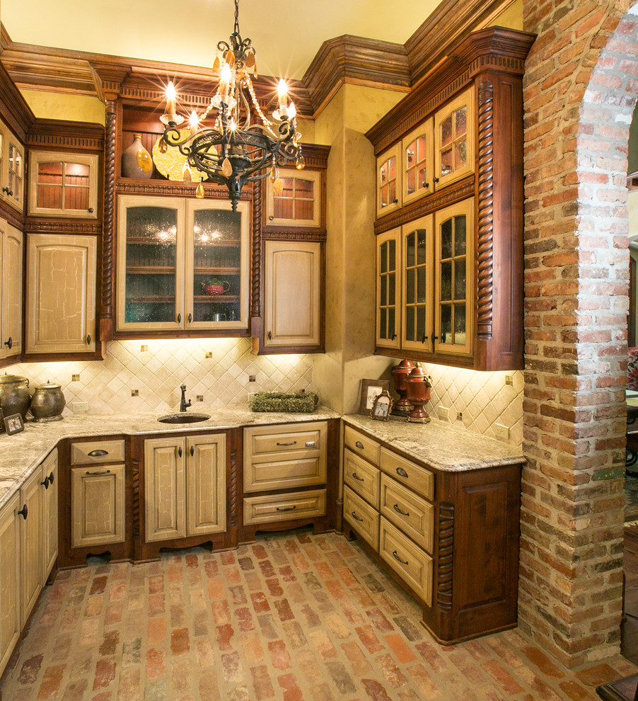 Inspiration for a mediterranean kitchen in New Orleans with an undermount sink, raised-panel cabinets, distressed cabinets, beige splashback and brick floors.