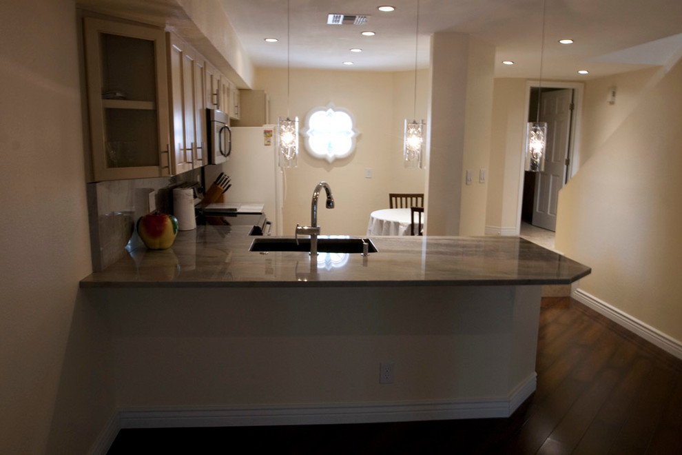 Example of a mid-sized transitional l-shaped dark wood floor and brown floor enclosed kitchen design in Phoenix with an undermount sink, shaker cabinets, light wood cabinets, granite countertops, beige backsplash, stone slab backsplash, stainless steel appliances and a peninsula