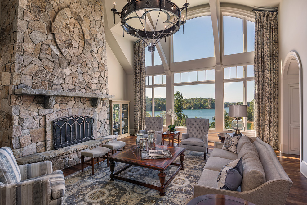Expansive traditional open concept living room in Other with a standard fireplace, a stone fireplace surround, grey walls, medium hardwood floors, a concealed tv and brown floor.