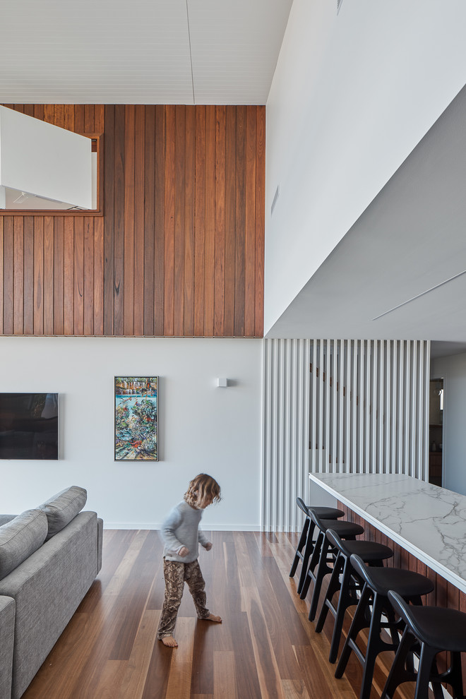 This is an example of a mid-sized beach style open concept living room in Gold Coast - Tweed with white walls, medium hardwood floors, a wall-mounted tv and brown floor.