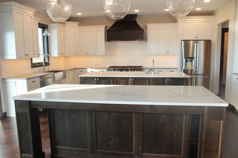 Inspiration for a large transitional l-shaped dark wood floor enclosed kitchen remodel with a farmhouse sink, shaker cabinets, white cabinets, quartz countertops, white backsplash, subway tile backsplash, stainless steel appliances and an island