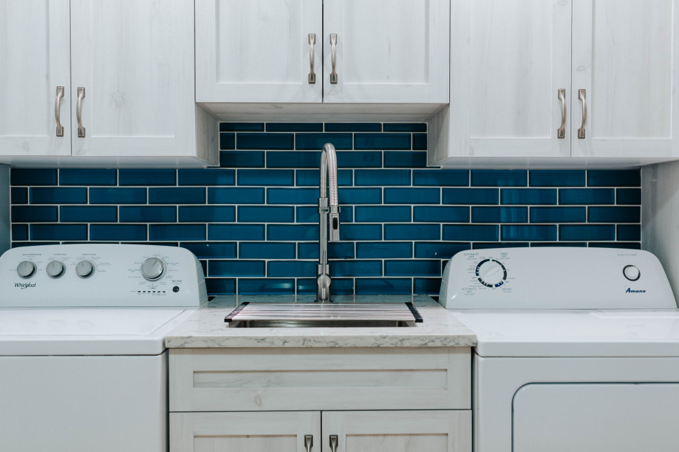 Mid-sized transitional utility room in Toronto with an undermount sink, shaker cabinets, grey cabinets, quartz benchtops, blue splashback, glass tile splashback, grey walls, medium hardwood floors, a side-by-side washer and dryer and grey benchtop.