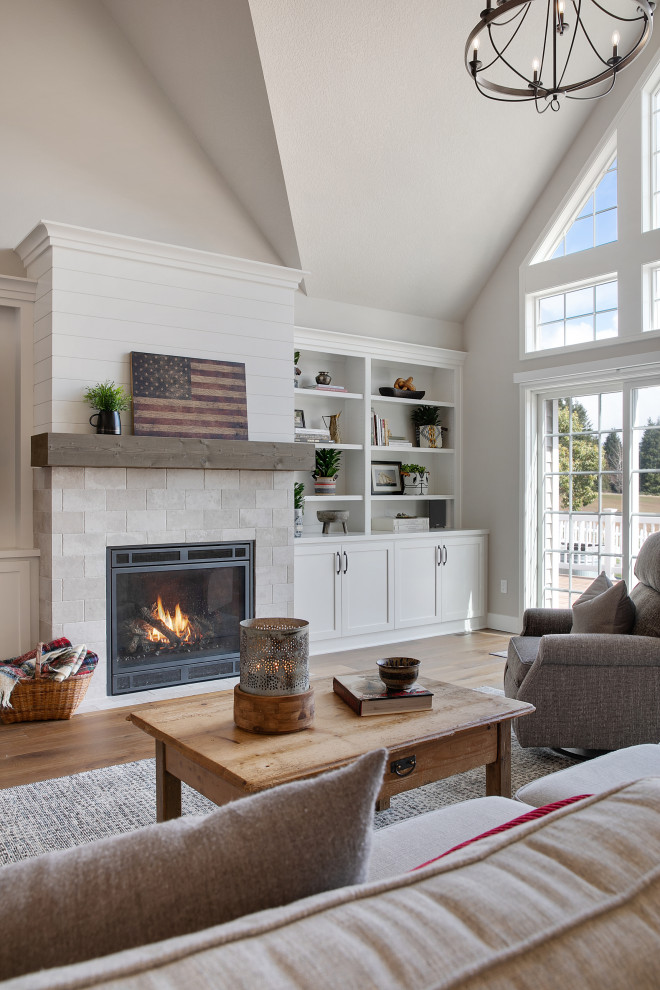 Photo of an expansive country open concept living room in Portland with grey walls, medium hardwood floors, a standard fireplace, a built-in media wall, brown floor and vaulted.