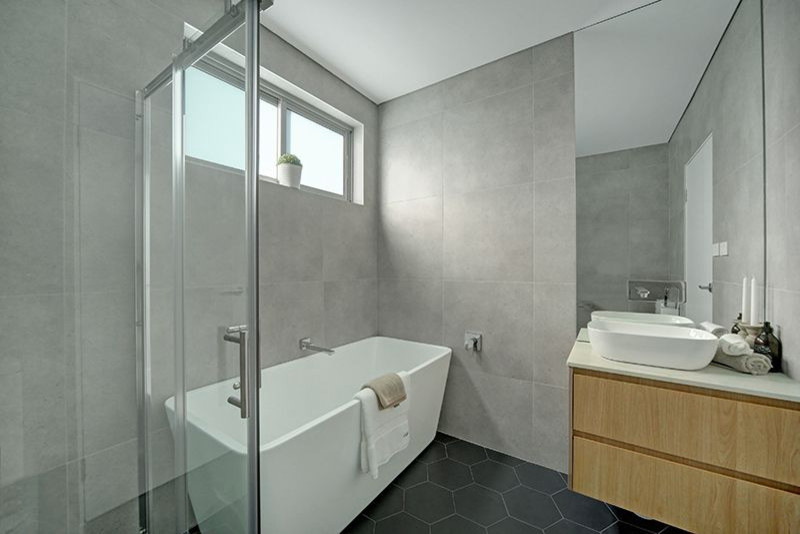Inspiration for a mid-sized modern 3/4 bathroom in Sydney with louvered cabinets, light wood cabinets, a two-piece toilet, porcelain floors, a console sink, marble benchtops, a freestanding tub, a corner shower, black tile, porcelain tile and grey walls.