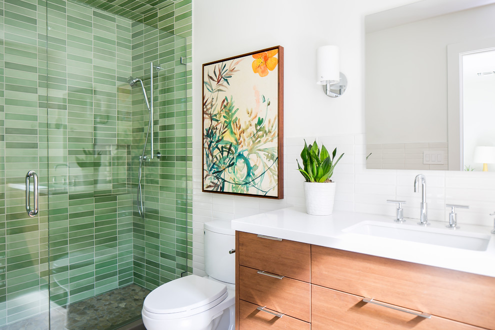 Midcentury 3/4 bathroom in Phoenix with medium wood cabinets, an alcove shower, green tile, white walls, engineered quartz benchtops, a hinged shower door, flat-panel cabinets, pebble tile floors, an undermount sink, grey floor and white benchtops.