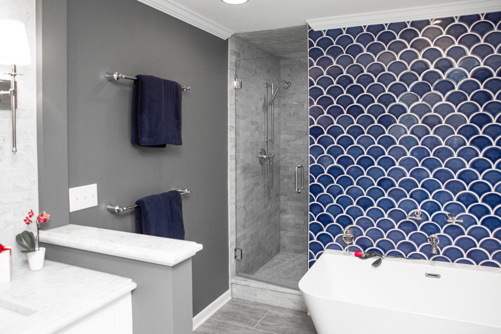 Photo of a mid-sized transitional master bathroom in Milwaukee with flat-panel cabinets, white cabinets, a freestanding tub, an alcove shower, a two-piece toilet, blue tile, mosaic tile, grey walls, porcelain floors, an undermount sink, marble benchtops, grey floor, a hinged shower door and grey benchtops.