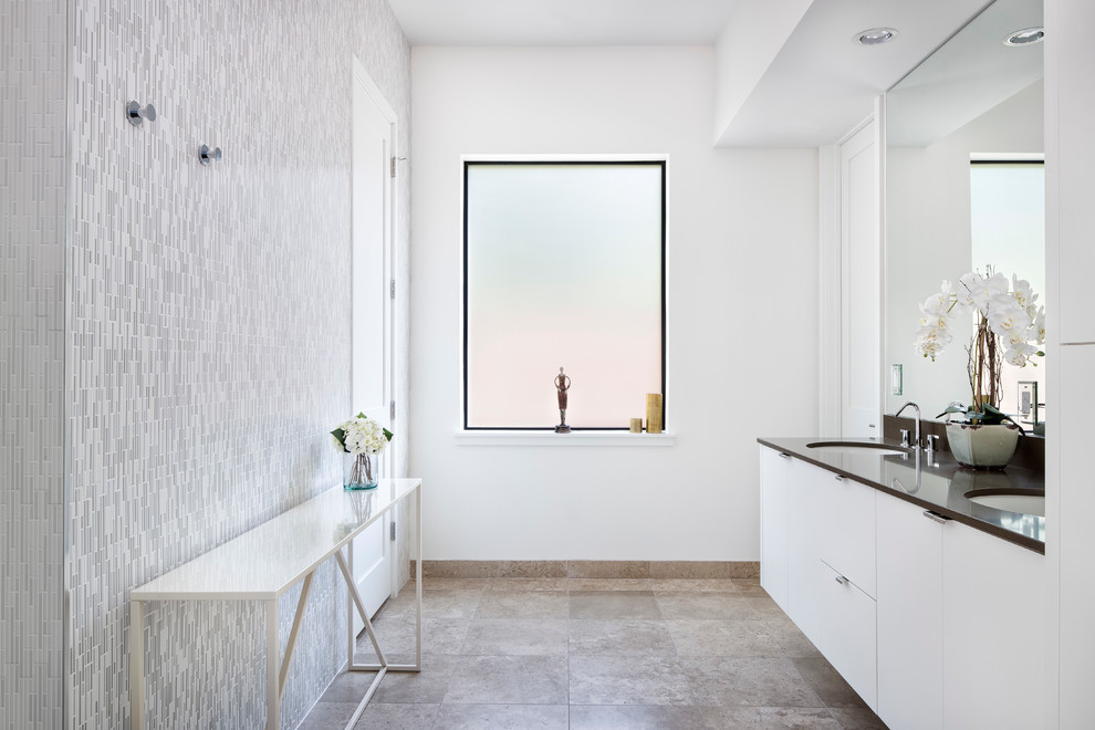 This is an example of a large contemporary master bathroom in Austin with flat-panel cabinets, white cabinets, gray tile, multi-coloured tile, white tile, mosaic tile, white walls, an undermount sink, travertine floors, solid surface benchtops and beige floor.