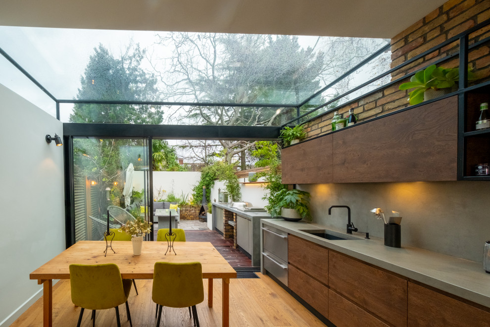 Small modern galley eat-in kitchen in London with an integrated sink, flat-panel cabinets, dark wood cabinets, concrete benchtops, grey splashback, cement tile splashback, stainless steel appliances, medium hardwood floors, with island, brown floor and grey benchtop.