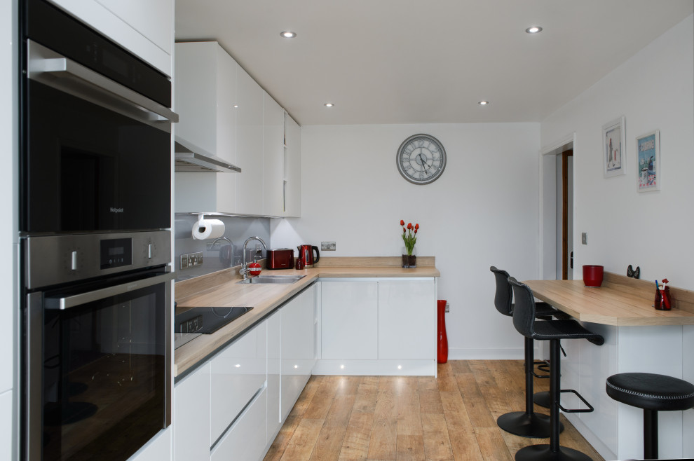 This is an example of a medium sized modern l-shaped open plan kitchen in Cornwall with a built-in sink, flat-panel cabinets, white cabinets, laminate countertops, metallic splashback, no island, beige worktops and feature lighting.