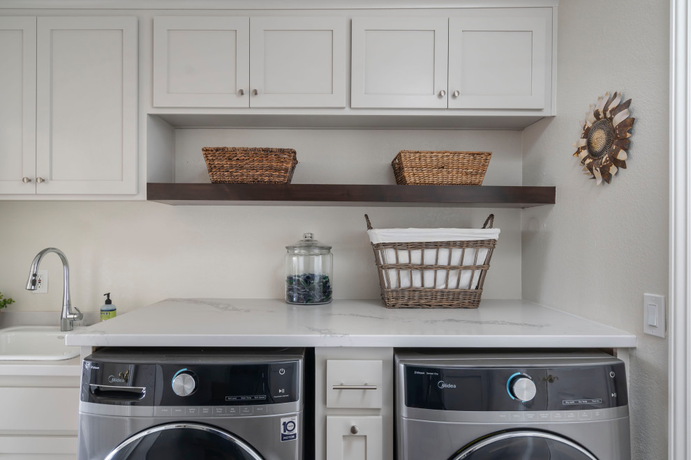 Photo of an expansive transitional single-wall laundry room in Los Angeles with a farmhouse sink, shaker cabinets, grey cabinets, quartz benchtops, grey splashback, ceramic splashback, vinyl floors, brown floor and white benchtop.