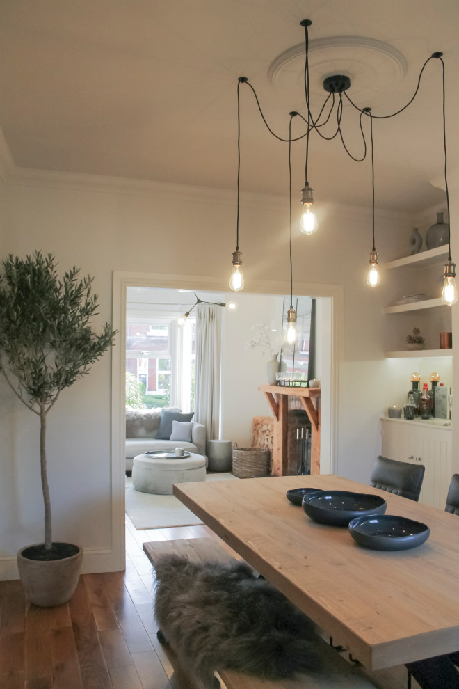 Cette image montre une salle à manger ouverte sur le salon urbaine avec un mur blanc, un poêle à bois, un manteau de cheminée en brique et un sol marron.