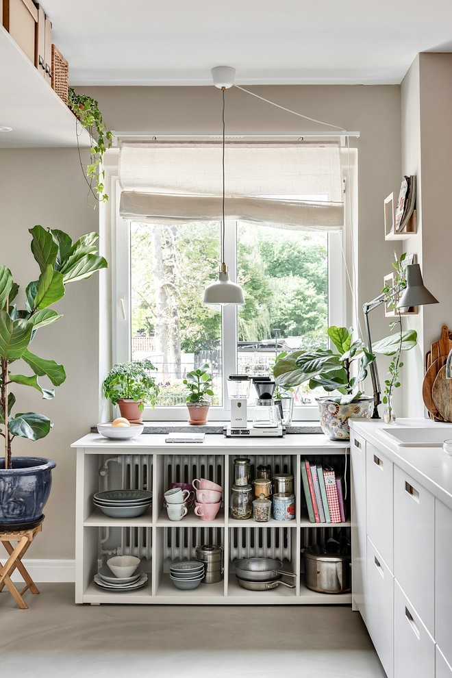 Photo of a small scandinavian l-shaped kitchen in Malmo with flat-panel cabinets, a drop-in sink, white cabinets, panelled appliances, concrete floors, grey floor and white benchtop.