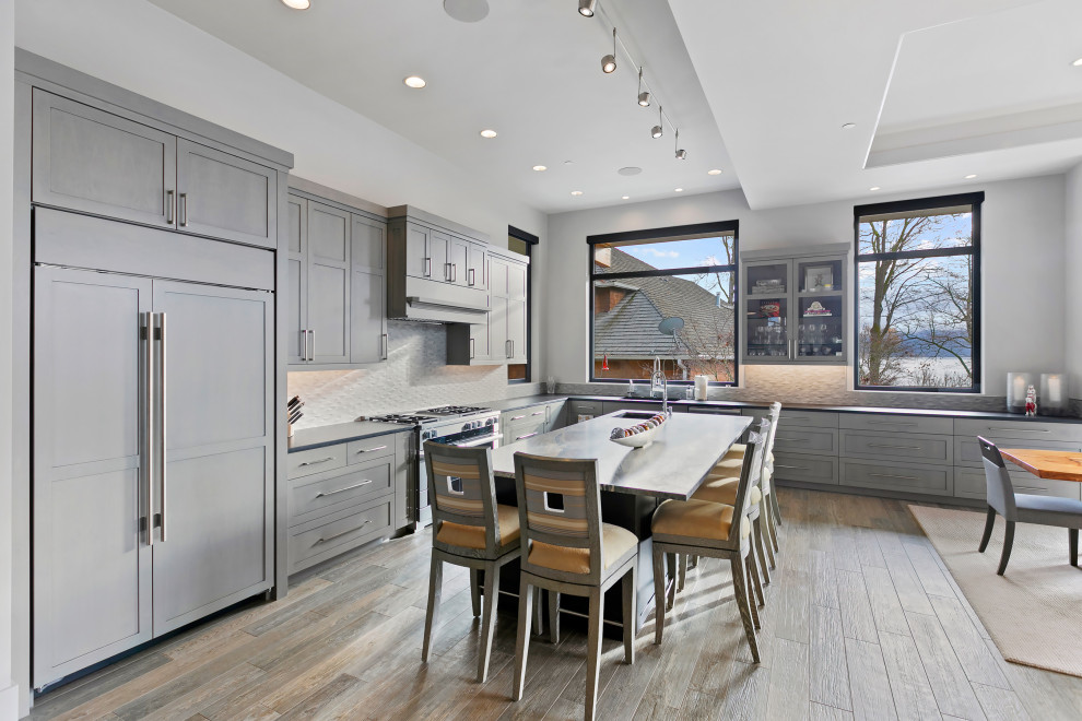 This is an example of an expansive transitional u-shaped open plan kitchen in Seattle with an undermount sink, recessed-panel cabinets, black cabinets, granite benchtops, grey splashback, porcelain splashback, stainless steel appliances, medium hardwood floors, with island, grey benchtop and coffered.
