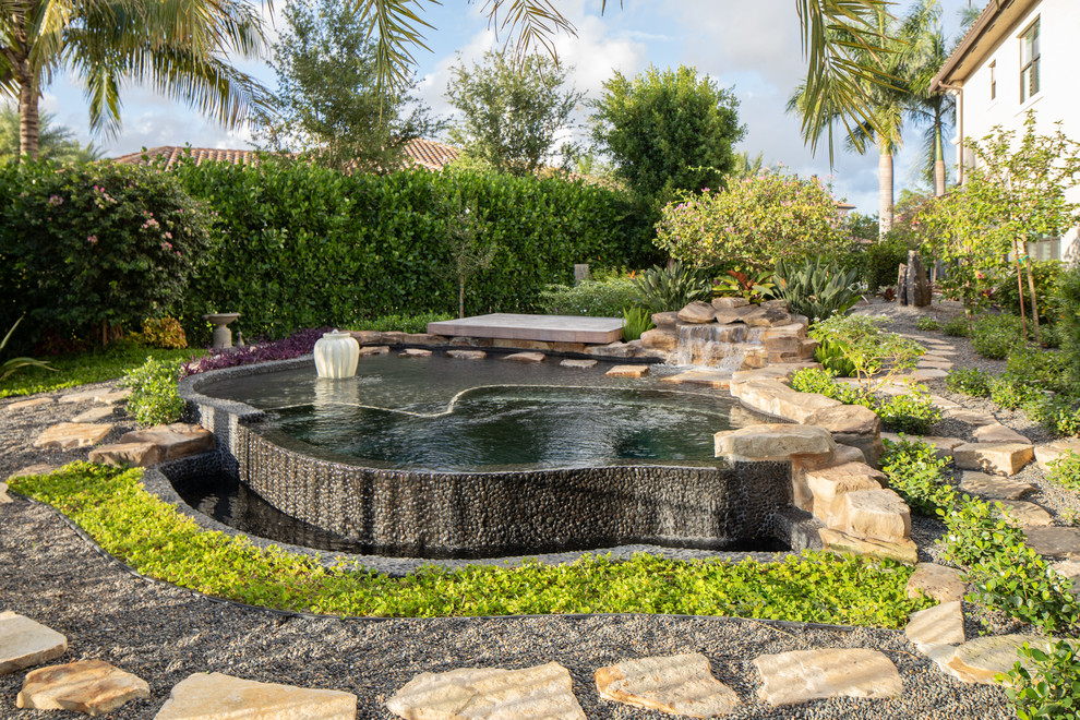 Design ideas for a mid-sized backyard custom-shaped natural pool in Miami with a hot tub and gravel.