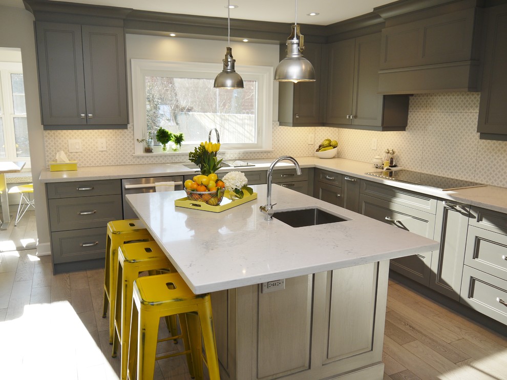 Inspiration for a mid-sized transitional l-shaped light wood floor enclosed kitchen remodel in Toronto with an undermount sink, recessed-panel cabinets, gray cabinets, quartz countertops, white backsplash, porcelain backsplash, stainless steel appliances and an island