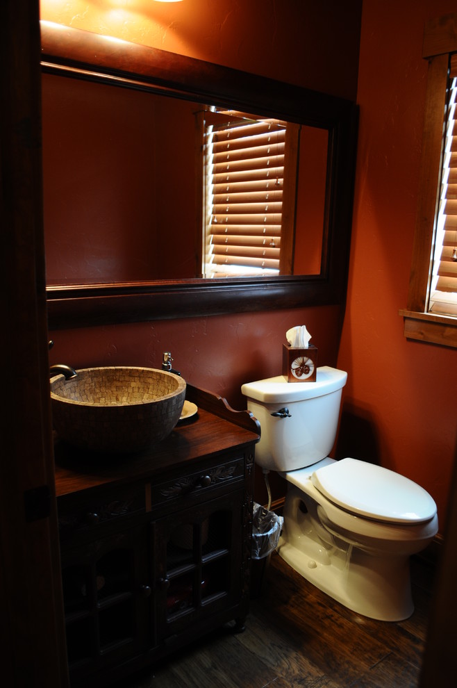 This is an example of a mid-sized country 3/4 bathroom in Denver with furniture-like cabinets, dark wood cabinets, red walls, dark hardwood floors, a vessel sink, a corner tub, an open shower, a one-piece toilet, red tile, wood benchtops and an open shower.