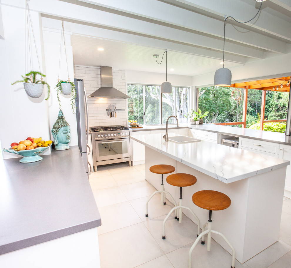 This is an example of a mid-sized eclectic u-shaped kitchen pantry in Gold Coast - Tweed with a farmhouse sink, shaker cabinets, white cabinets, white splashback, subway tile splashback, stainless steel appliances, porcelain floors, with island, white floor and multi-coloured benchtop.