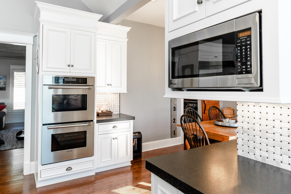 Bild på ett stort funkis svart svart kök, med en rustik diskho, luckor med infälld panel, vita skåp, bänkskiva i kvartsit, vitt stänkskydd, stänkskydd i marmor, rostfria vitvaror, mellanmörkt trägolv, en köksö och brunt golv