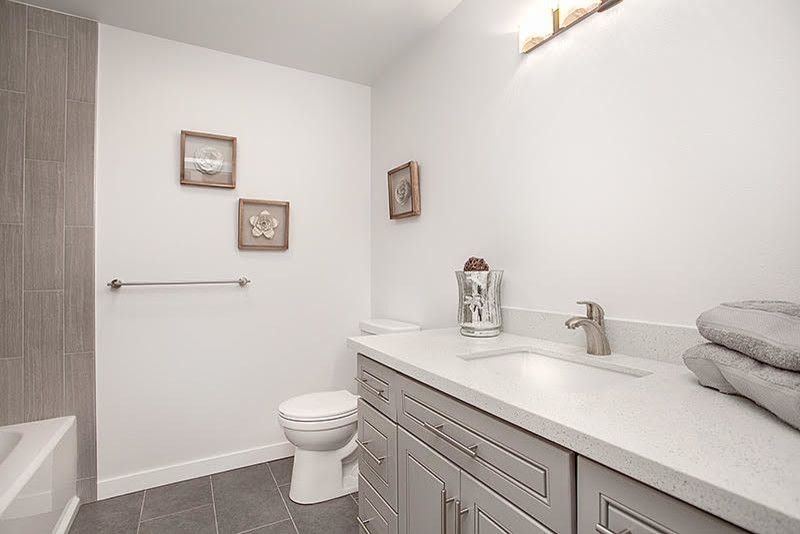 Example of a transitional gray tile and porcelain tile porcelain tile alcove bathtub design in Seattle with raised-panel cabinets, gray cabinets, a one-piece toilet, white walls, an undermount sink and quartzite countertops