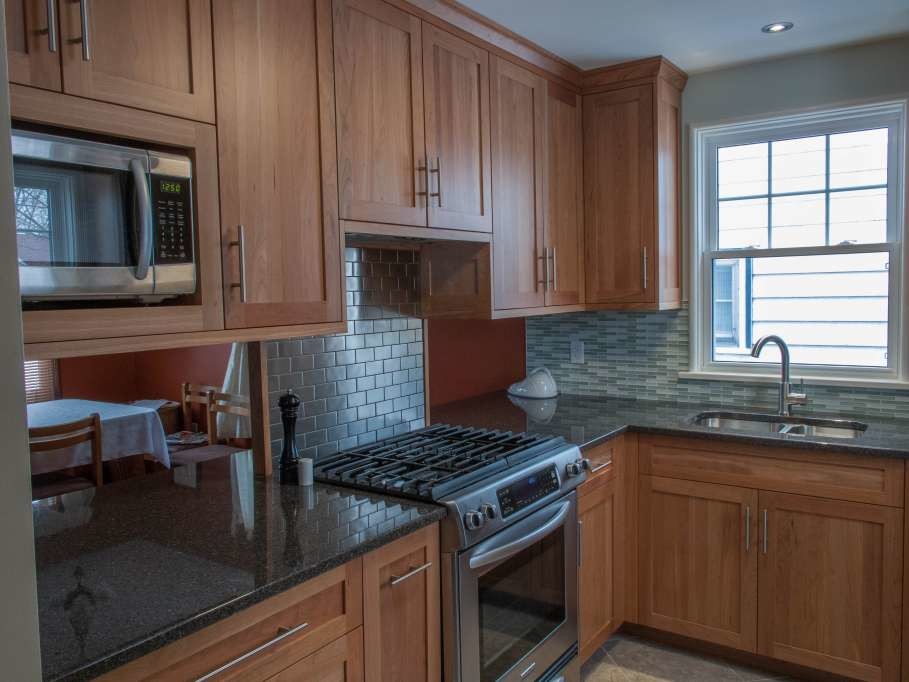 Enclosed kitchen - small transitional u-shaped porcelain tile and beige floor enclosed kitchen idea with an undermount sink, shaker cabinets, light wood cabinets, granite countertops, green backsplash, glass tile backsplash, stainless steel appliances and a peninsula